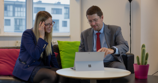 Eine blonde Frau und ein Mann schauen lächelnd auf einen Surface Bildschirm.